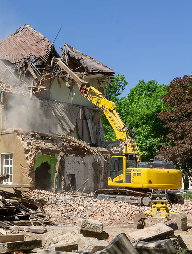 Big yellow excavator breaks down old house at summer