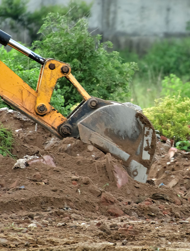 Excavator is working with dusty red soil.