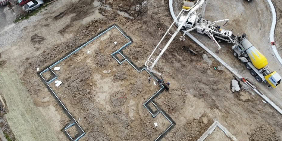 Aerial view of a concrete mixer truck and pump equipment pouring concrete into the laid-out foundation walls of a building project.